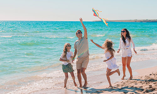 Family of four playing with kite on beach with blue ocean water and sand behind them.