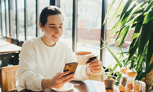 Young man sitting in cafe using cell phone and holding credit card in hand.