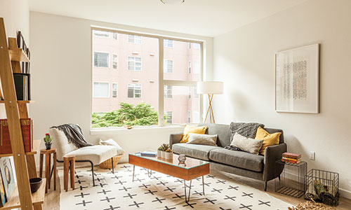 Modern living room with couch, chair, small coffee table, bookshelf, and large window with a lot of natural light.