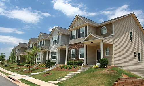 Row of townhomes from street view with green grass and blue cloudy skies.